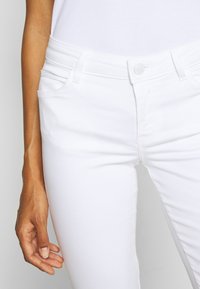 Witte spijkerbroek van denim met een slanke pasvorm, ontwerp met vijf zakken en zilveren knoopsluiting, met een gladde textuur en minimale stikdetails.