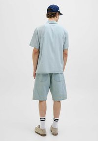 Camisa de cuello corta de manga corta en azul claro con un patrón de cuadrícula sutil, combinada con pantalones cortos de mezclilla azul claro, calcetines blancos con rayas negras y zapatos beige.