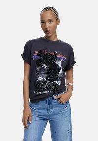 Grafisches T-Shirt aus dunkelgrauer Baumwolle mit einem Pailletten-Mosaik-Design von Mickey Mouse und Text. Mit umgekrempelten Ärmeln und lockerer Passform; kombiniert mit hellblauen Jeans.