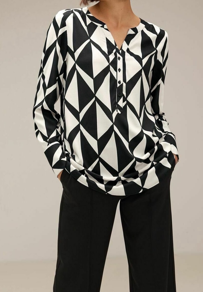Top a maniche lunghe con motivo geometrico in bianco e nero, colletto a punta, pattina con bottoni e vestibilità comoda, abbinato a pantaloni neri.