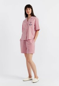 Ensemble comprenant une chemise à manches courtes rayée rouge et blanche et un short, avec une poche avant dotée d'un petit détail brodé sur le thème nautique.