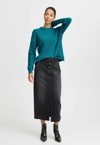 Pull en tricot teal avec texture côtelée, associé à une jupe midi en denim noir avec une fente à l'avant et des bottines noires.