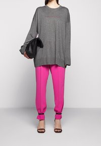 Gray long-sleeve sweater with a pink accent, paired with bright pink tapered pants. Black clutch and strappy black heels complete the look.