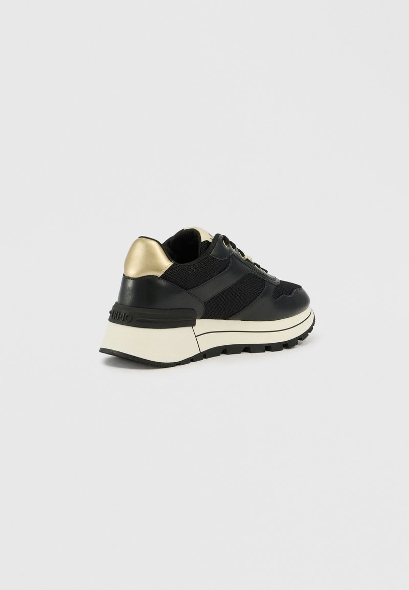 Schwarzer Sneaker aus Mesh- und Leder-Material, mit einem goldenen Akzent an der Ferse und einer dicken weißen Sohle für zusätzlichen Halt.