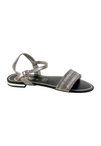 Sandalias planas de metal plateado con una tira ancha texturizada, correa ajustable en el tobillo y suela negra con un contorno blanco.