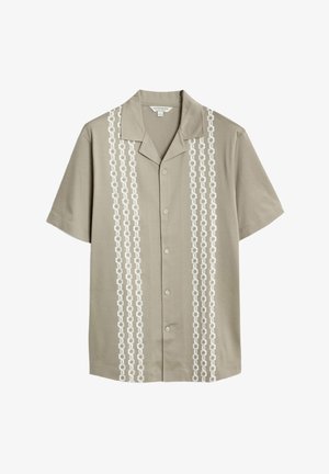 Koszula khaki z krótkim rękawem z białym wzorem w łańcuch wzdłuż przodu. Posiada kołnierz typu camp i zapięcie na guziki; wykonana z lekkiego materiału.