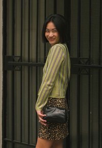 Suéter recortado a rayas verdes y azules, combinado con una mini falda marrón de estampado de leopardo y un pequeño bolso negro. Materiales texturizados visibles.