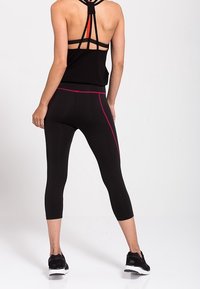 Leggings sportive neri con strisce rosa ai lati, abbinati a un top a canottiera nero con spalline. Realizzati in un tessuto elastico e traspirante; design aderente.