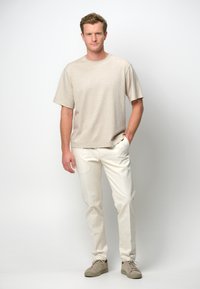 Beige kortärmad T-shirt i avslappnad passform, kombinerad med krämfärgade, avsmalnande byxor och ljusbeige sneakers. Enkelt design och mjuk textur.