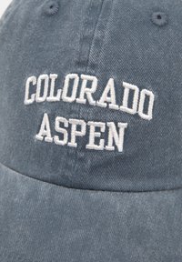 Modrá rifľová čiapka s nastaviteľným pásikom, so bielym výšivkovým nápisom "COLORADO ASPEN" na prednej strane. Nápis je tučný a je napísaný veľkými písmenami.