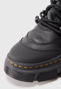 Black leather ankle boot featuring a rounded toe, thick black sole with yellow stitching, and black laces. Textured upper with slight shine.