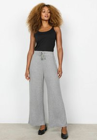 Grijze wijde sweatpants met een koord in de taille, zachte textuur, gecombineerd met een zwart tanktop en zwarte schoenen.