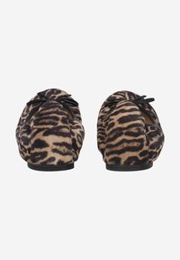 Des chaussures plates avec un motif animal beige et noir, en daim doux, dotées d'un accent en forme de nœud noir sur le devant.