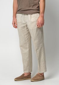 Linnenbyxor i ljusbeige, med avslappnad passform, framfickor och sidofickor, kombinerat med bruna slip-on skor.