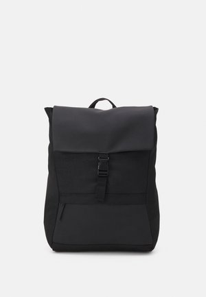 Black backpack with top flap secured by a central buckle, front zippered pocket, and a small carrying handle on top.