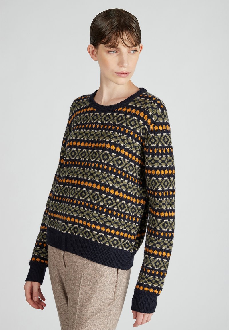 Granatowy sweter w geometryczne wzory w kolorze pomarańczowym i zielonym. Okrągły dekolt, luźny krój i ściągacze. Miękka faktura i szczegółowy wzór dzianiny.