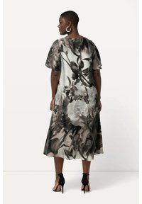 Blumendruckkleid in Schwarz-, Weiß- und Grautönen, mit einem knielangen Saum, kurzen Ärmeln und einer fließenden Silhouette. Schwarze Absatzsandalen.