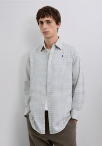 Koszula na guziki w lekkim materiale, z niebiesko-żółtym wzorem w kratę, białymi guzikami oraz logo na piersi na jasnym tle.