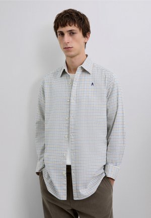 Camisa de botones con tejido ligero a cuadros, con patrón de cuadrícula azul y amarillo, botones blancos y un logo en el pecho sobre un fondo claro.