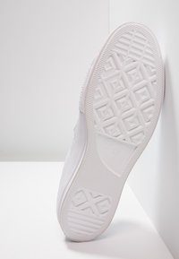 Semelle de chaussure en toile blanche avec caoutchouc texturé pour l'adhérence, présentant un motif en losange et le logo "Converse All Star" sur le talon.