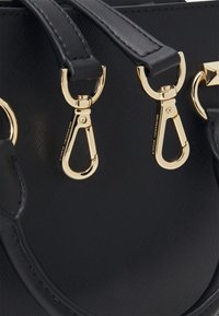 Sort tekstureret læderhåndtaske med to guldfarvede låse fastgjort til sorte læderhåndtag.