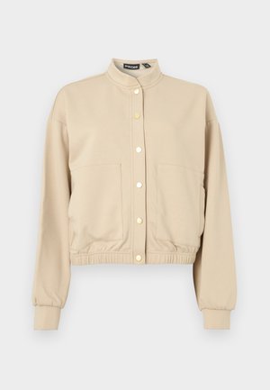 Beige cropped jacket made of soft fabric, featuring a stand collar, two front pockets, gold snap buttons, and elasticized hem and cuffs.