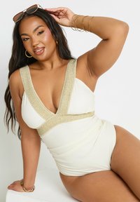 Kermanvärinen yksiosainen uimapuku, jossa syvä V-pääntie, kullanväriset teksturoidut nauhat hartioissa ja vyötäröllä sekä pehmeät rypytykset sivuilla.