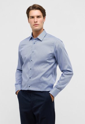 Blauw gestippeld overhemd met een button-down kraag, met een geometrisch patroon en lange mouwen, gecombineerd met een donkere broek.