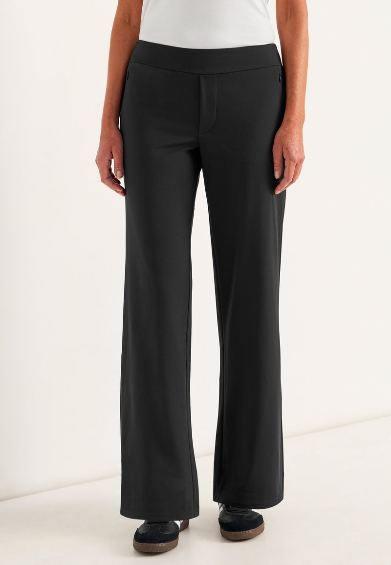 Zwarte, wijde broek in een soepele, rekbare stof met een hoge tailleband, voorzien van een voornaad en zijzakken. Gestyled met donkere schoenen.