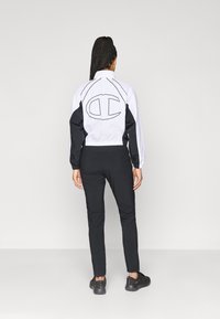 Juodai baltas vėjui atsparus švarkas su elastingais rankogaliais ir juosmeniu, su dideliu logotipu ant nugaros. Suderintas su juodais siaurais džinsais.