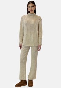 Beige geribbelde gebreide trui en broekset met een hoge halslijn. Zachte textuur, losse pasvorm, gecombineerd met bruine suède enkellaarzen.