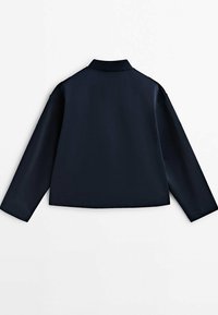 Veste courte bleu marine avec col, manches longues et texture lisse. Présente un design minimaliste sans fermetures ni ornements visibles.