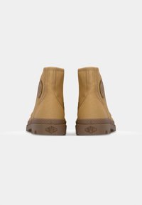 Botas de tobillo de lona color beige con punta redondeada, acentos laterales texturizados y suela de goma marrón con un agarre estampado. Detalle del logo en la parte trasera.