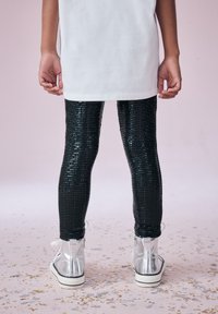 Leggings neri con paillettes abbinati a una tunica bianca, completati da stivaletti argentati lucidi con cerniere e suole a righe nere.