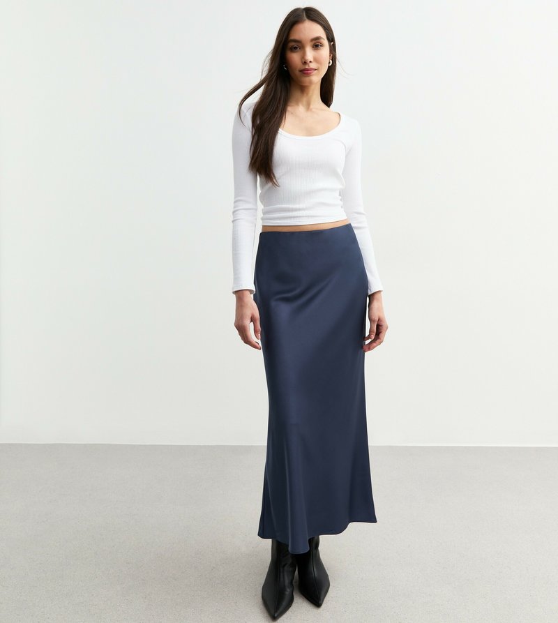 Vit långärmad ribbat topp i kombination med en marinblå satin maxikjol. Spetsiga svarta klackstövlar fulländar outfiten. Slät textur och åtsittande silhuett.