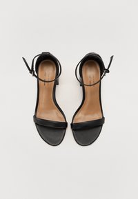 Sandales noires à bout ouvert avec brides à la cheville et talons blocs bas sur un fond clair uni.