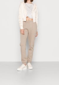 Kort beige hoodie med texturerade ärmar, ljusgrå tie-dye t-shirt, beige avsmalnande sweatpants och vita sneakers med iriserande detaljer.