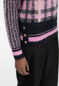 Maglione in maglia con motivo a quadri rosa e nero, maniche testurizzate, base blu navy e bottoni decorativi dorati sui lati.