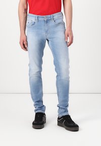 Lichtblauwe spijkerbroek met een slim fit, voorzien van vijf zakken, een knoopsluiting en subtiele vervaging op de bovenbenen. Zwarte sneakers gedragen.