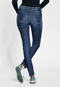 Skinny blue denim jeans with a faded wash, five pockets, and contrast stitching. Paired with white and green sneakers.