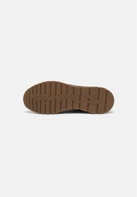 Semelle de chaussure avec une bande de roulement en caoutchouc marron présentant des rainures horizontales et le mot "Tamaris" embossé au bas.