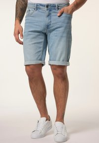 Lysblå denimshorts med oprevet kant, der har forlommer og knaplukning. Bæret med hvide sneakers.