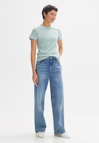 T-shirt azzurro chiaro attillato con maniche corte, abbinato a jeans blu a gamba ampia. I jeans presentano una finitura sbiadita e una chiusura con bottone.