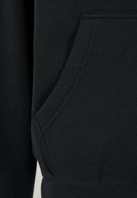 Gros plan d'une poche de sweat à capuche en tissu noir avec couture visible et ceinture côtelée en bas.