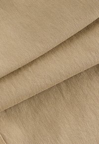 Beige stof met een textuur oppervlak, met opgevouwen lagen die een subtiel geweven patroon tonen. Licht, zacht materiaal met een matte afwerking.