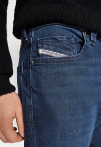 Dunkelblaue Jeans aus Denim mit strukturierter Oberfläche, ausgestattet mit einem auffälligen Rückentaschenlabel und einem klassischen Bund mit Knopf- und Reißverschluss.