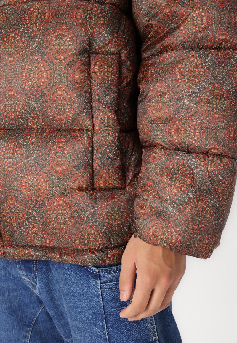 Gepolsterte Jacke mit aufwendigem mehrfarbigem geometrischem Muster in Rost, Grün und Rot. Besitzt eine kastige Form und einen elastischen Saum.