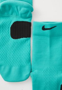 Ein Paar türkisfarbener Sportsocken mit schwarzem Nike-Swoosh und gepolsteter Sohle, sichtbar vor einem weißen Hintergrund.