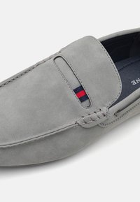 Mocassins en daim gris avec un design à enfiler, présentant de subtils détails de couture et une bande colorée près de l'ouverture. Texture lisse.