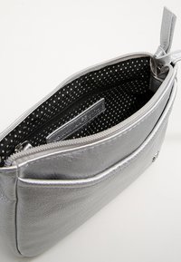 Srebrna metaliczna saszetka o gładkiej fakturze, z zamknięciem na zamek i wnętrzem w kropki. Posiada małą metkę w środku.